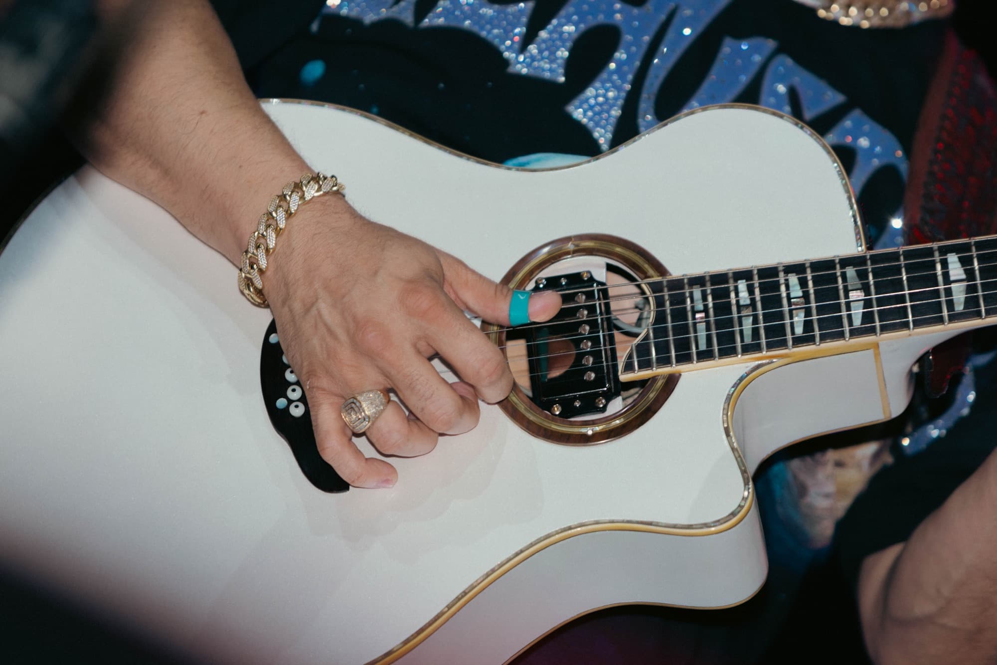 Hand with gold rings picking the white guitar
