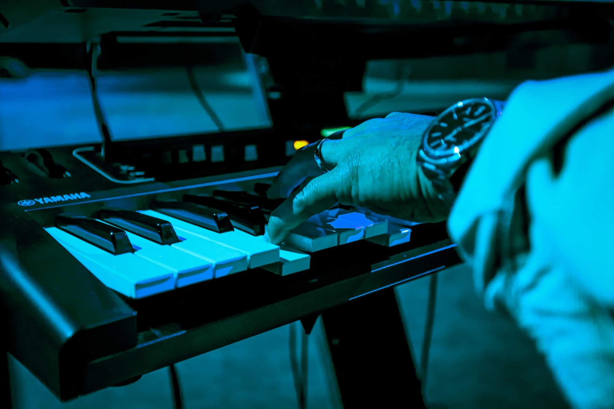 Hand on the synth keys in teal light