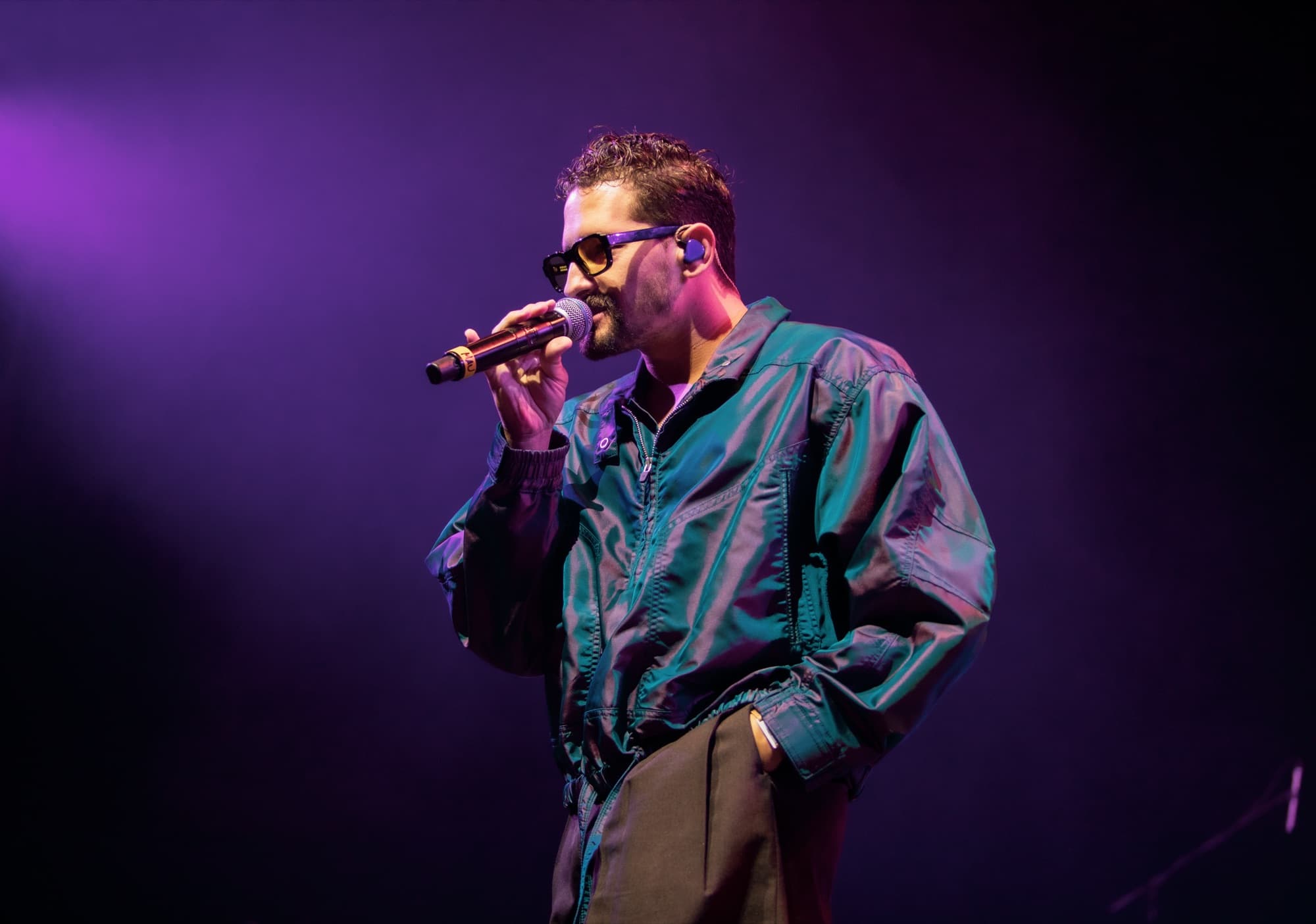 Guaynaa in an iridescent bomber and sunglasses singing into the mic