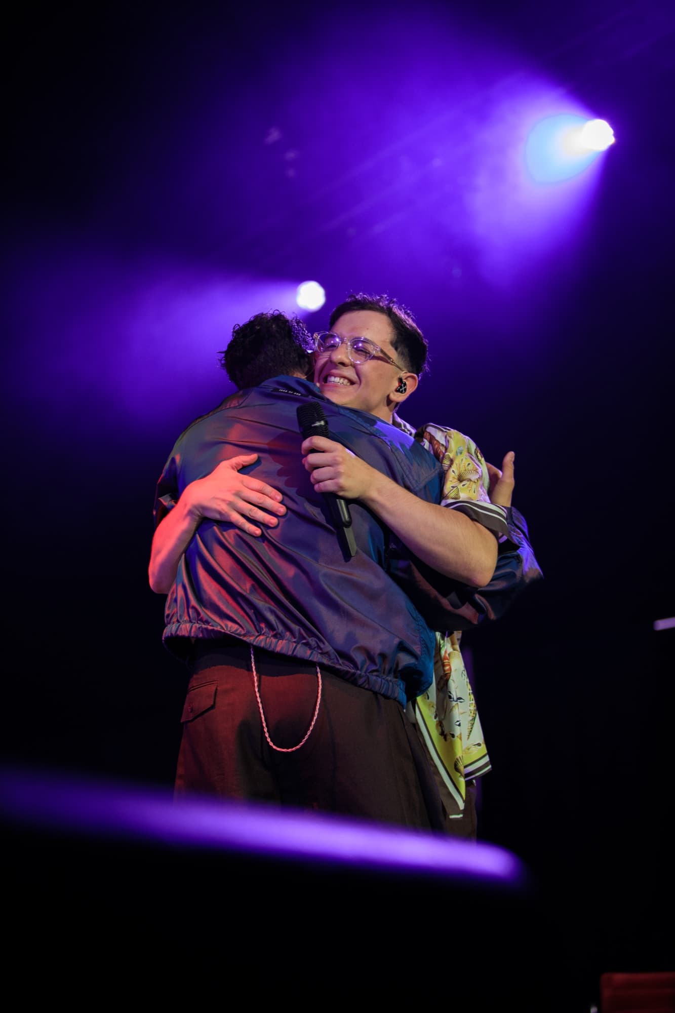 Two artists embracing on stage under purple haze