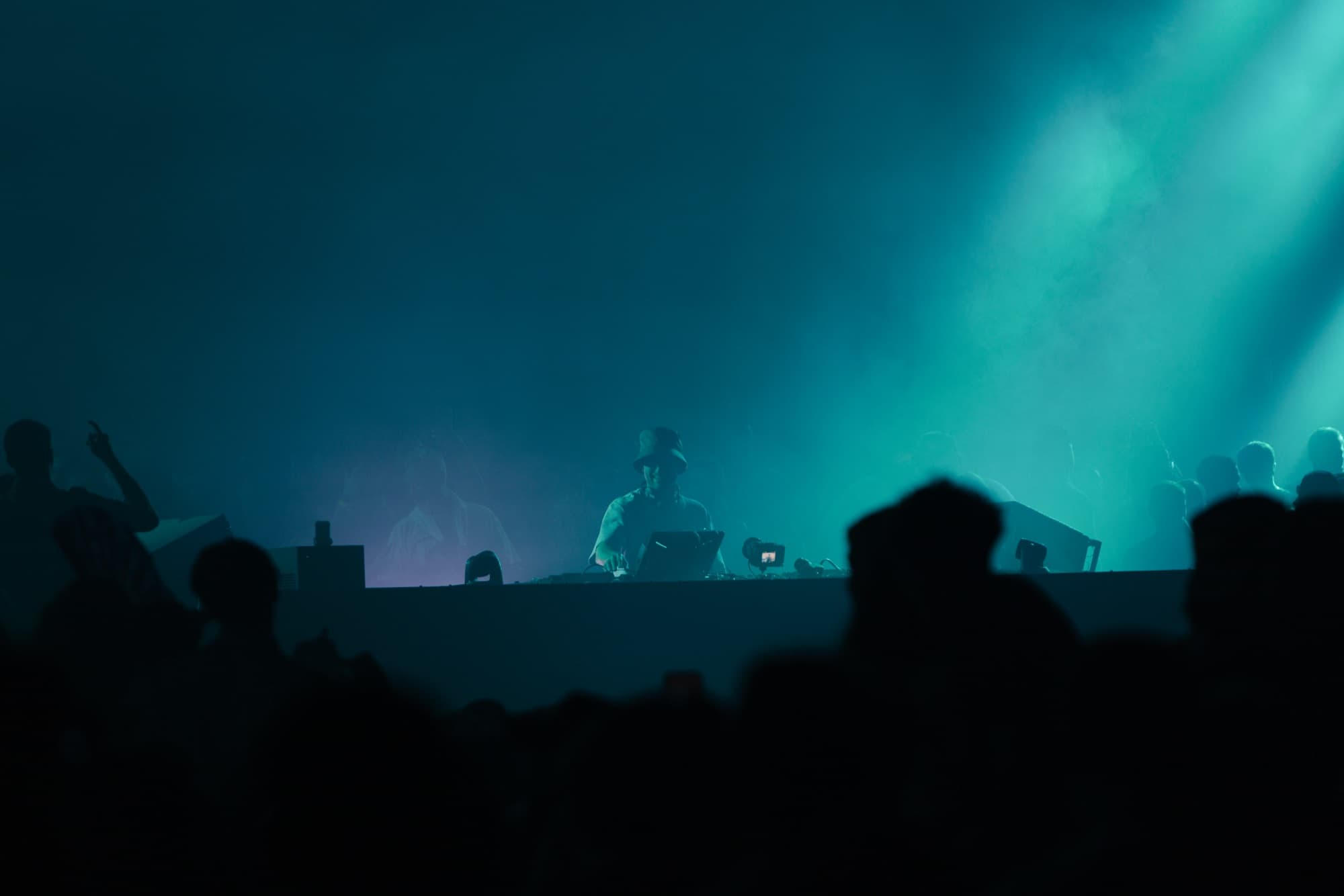 DJ silhouetted in teal light above the crowd