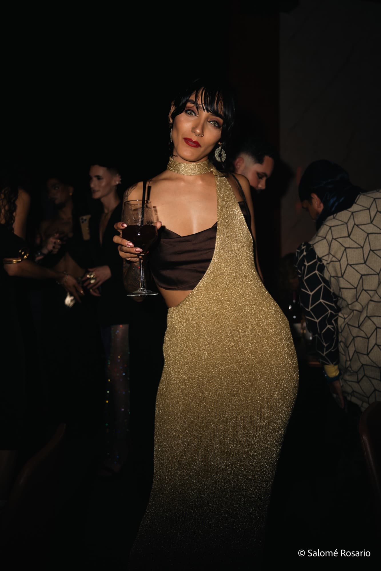 Woman in a gold dress raising a glass of wine at a party