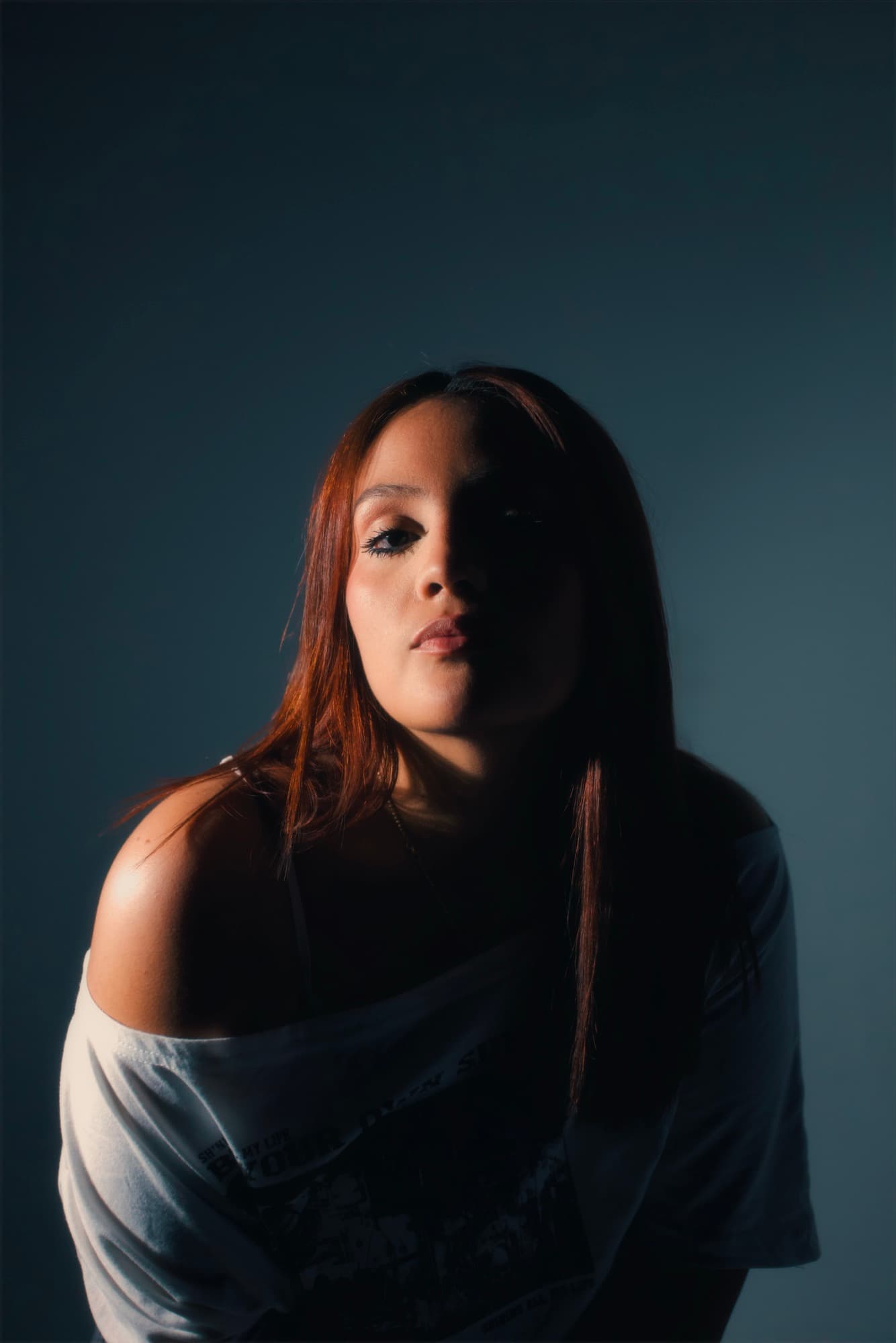 Moody studio portrait of Salomé Rosario with red hair against a slate backdrop