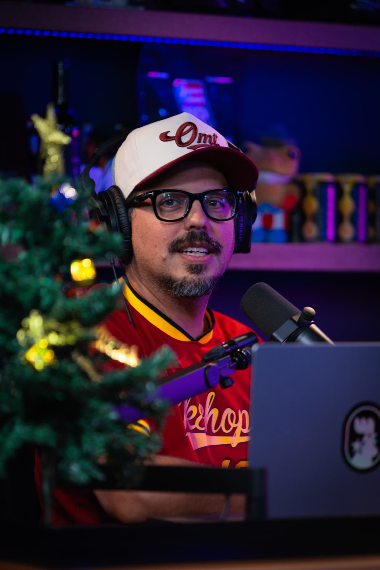 Podcast host at the mic under neon set lights